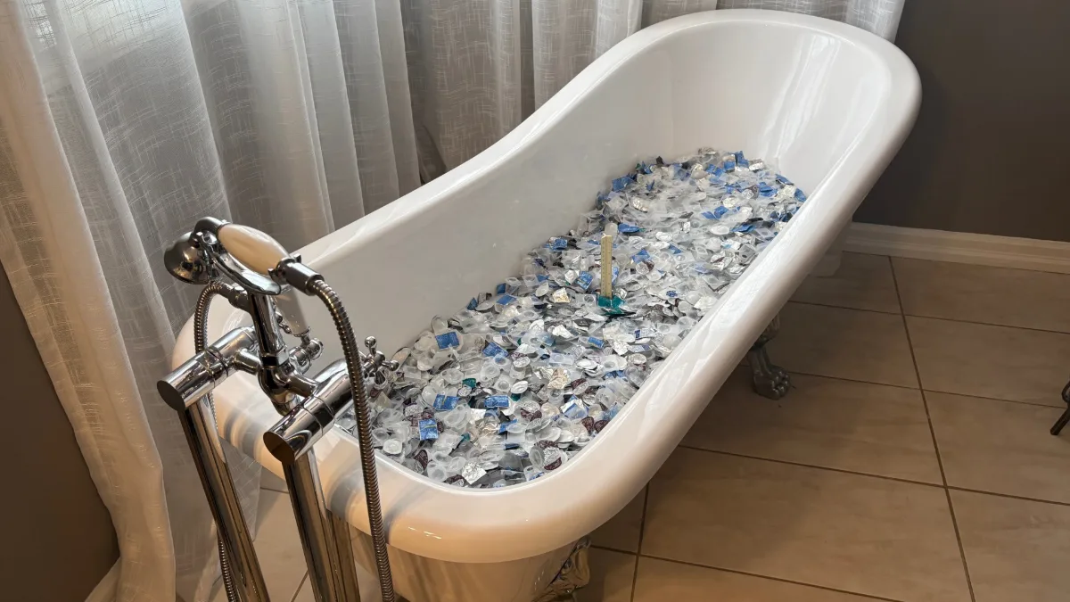 A clawfoot bathtub filled with 7,244 used contact lens blister packs, representing one year of waste from just 10 daily lens wearers